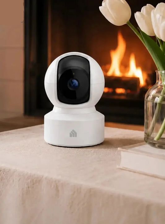 White security camera on a table with a fireplace and flowers in the background