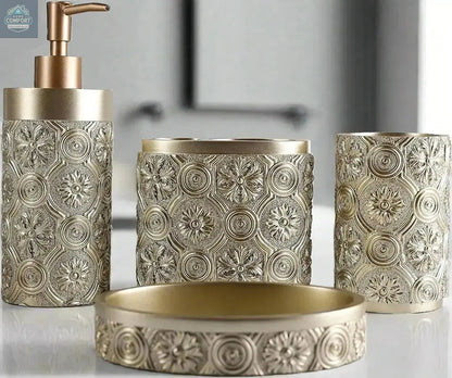 Gold ornate patterned bathroom accessories set with soap dispenser, toothbrush holder, tumbler, and soap dish on countertop
