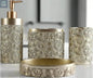 Gold ornate patterned bathroom accessories set with soap dispenser, toothbrush holder, tumbler, and soap dish on countertop