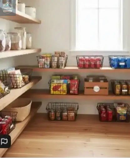 Organized farmhouse pantry with black wire storage baskets holding snacks, canned drinks, and pantry goods on wooden shelves.