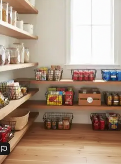 Organized farmhouse pantry with black wire storage baskets holding snacks, canned drinks, and pantry goods on wooden shelves.