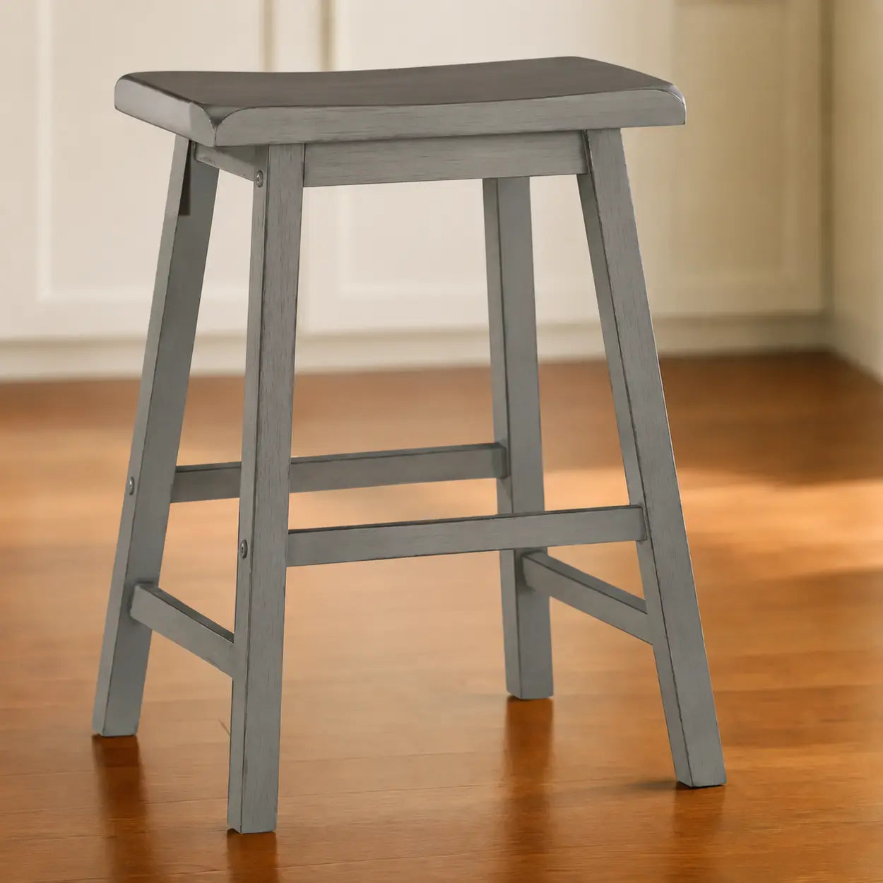 Single grey wood backless counter stool with saddle seat shown on indoor floor