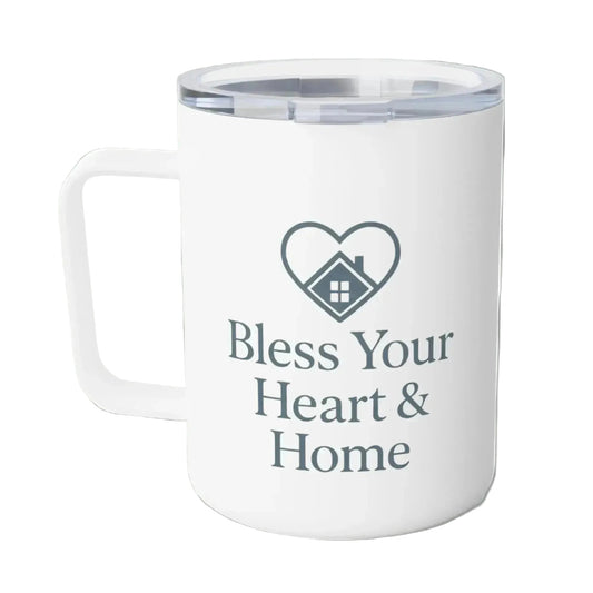 A white insulated travel mug with a clear lid, featuring a dark gray heart-shaped house graphic and the text 'Bless Your Heart & Home' printed on the front.