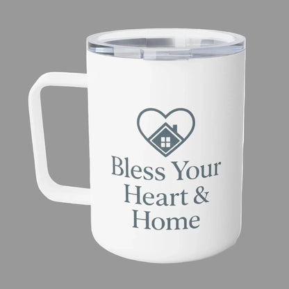 A white insulated travel mug with a clear lid, featuring a dark gray heart-shaped house graphic and the text 'Bless Your Heart & Home' printed on the front.