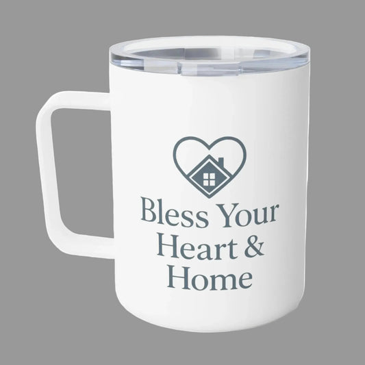 A white insulated travel mug with a clear lid, featuring a dark gray heart-shaped house graphic and the text 'Bless Your Heart & Home' printed on the front.
