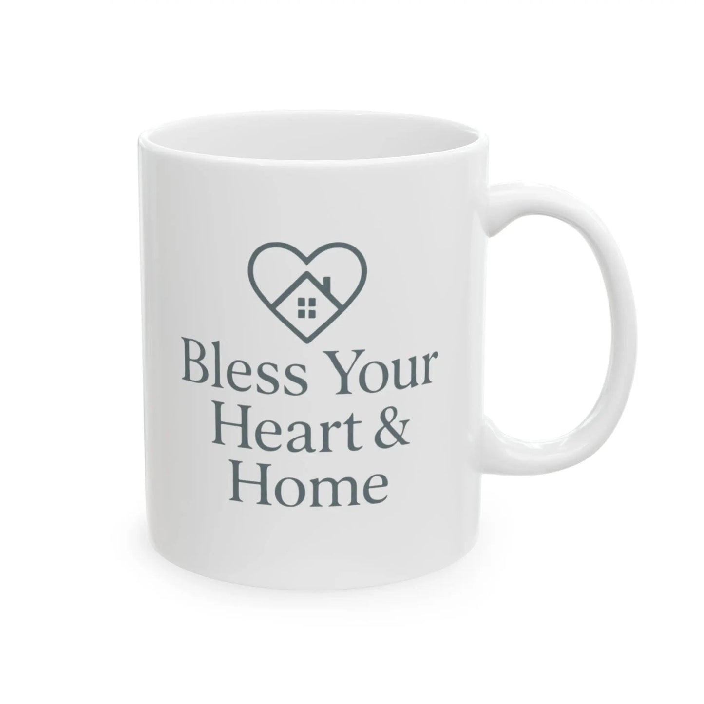 A white ceramic mug with a dark gray printed design featuring a heart outline containing a small house and the text 'Bless Your Heart & Home'.