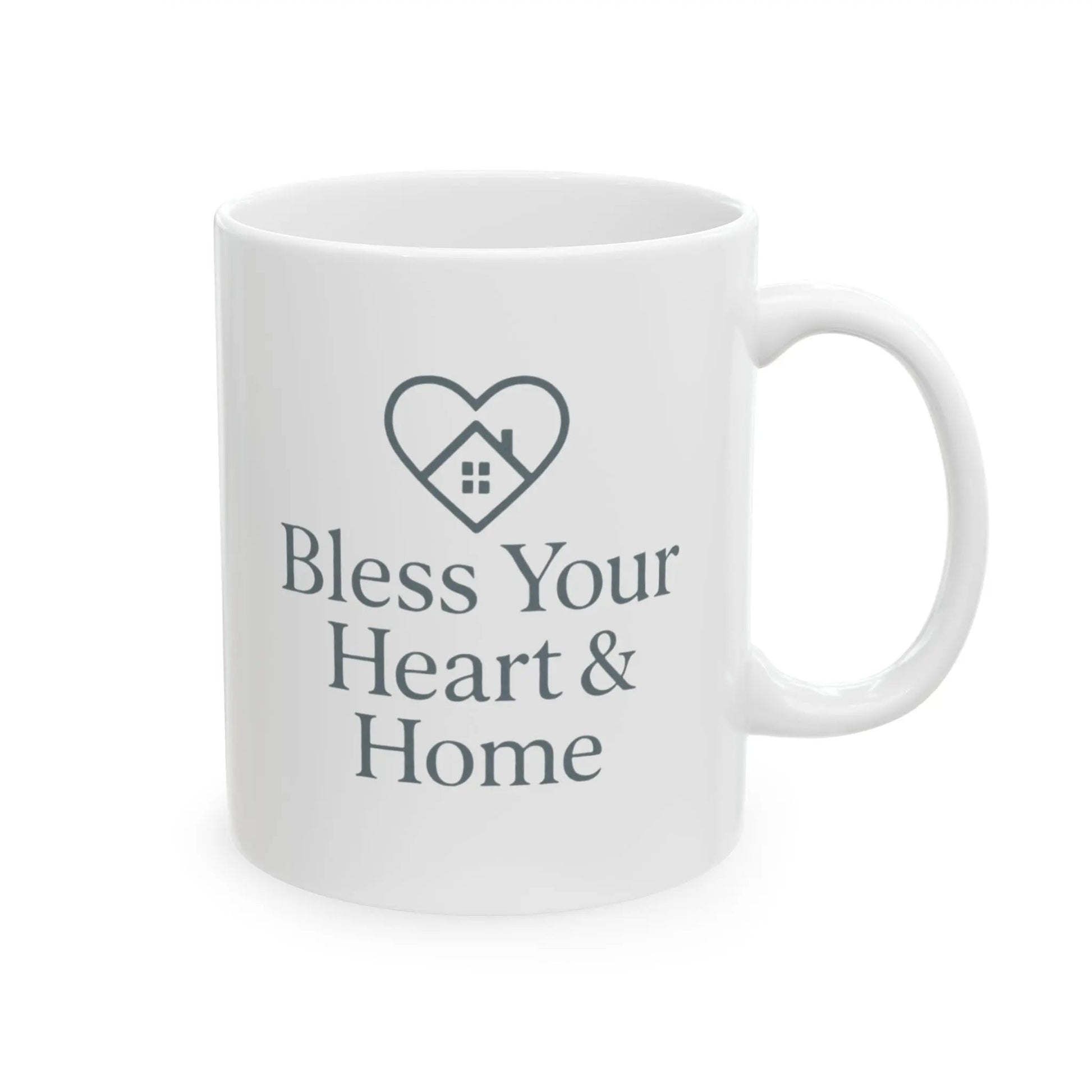 A white ceramic mug with a dark gray printed design featuring a heart outline containing a small house and the text 'Bless Your Heart & Home'.