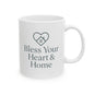 A white ceramic mug with a dark gray printed design featuring a heart outline containing a small house and the text 'Bless Your Heart & Home'.