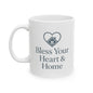 A white ceramic mug with a dark gray printed design featuring a heart outline enclosing a small house and the text 'Bless Your Heart & Home'.