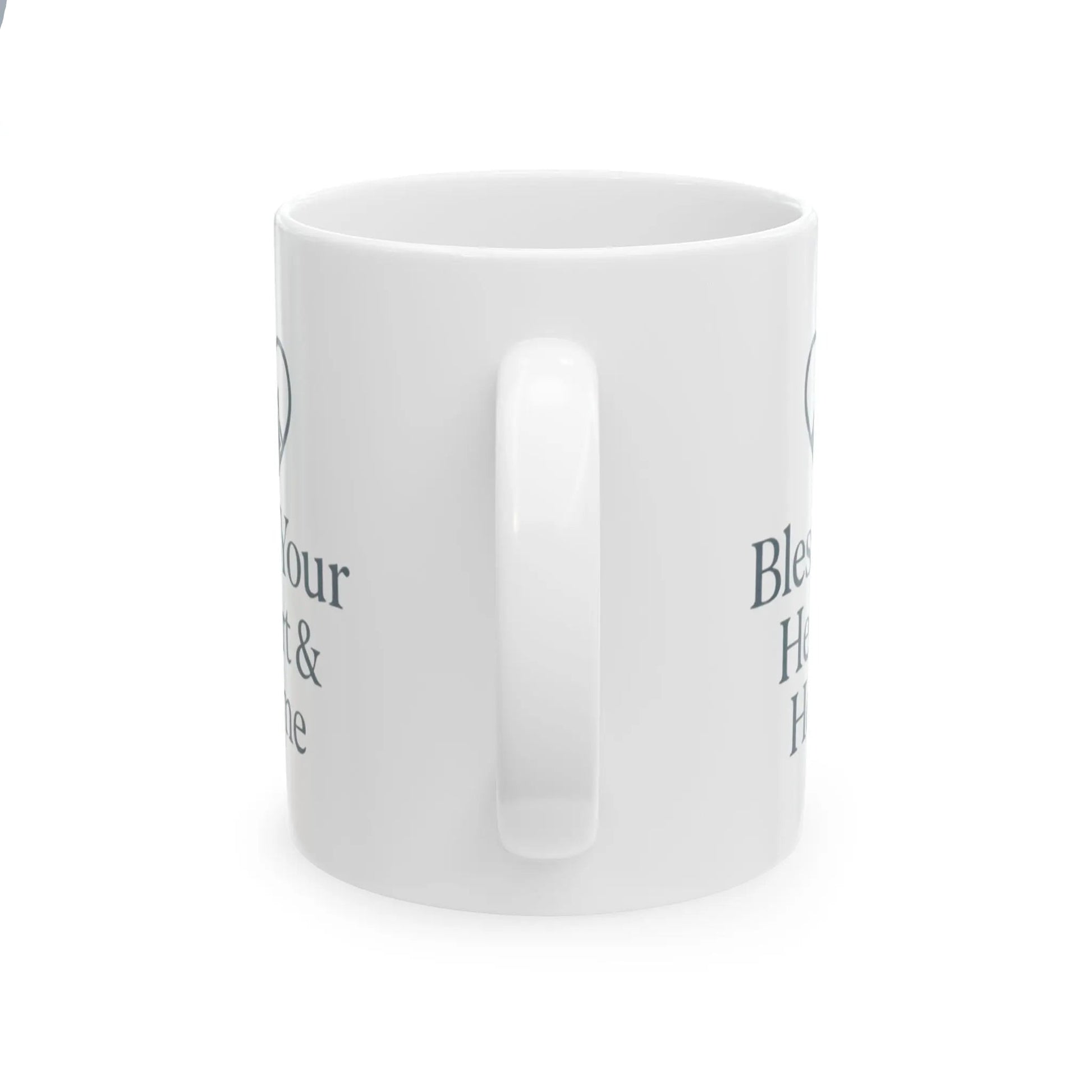 A white ceramic mug with a glossy finish, shown from a side angle on a white background. The mug features dark gray text partially visible on both sides, including the words 'Bless' and 'Home'.