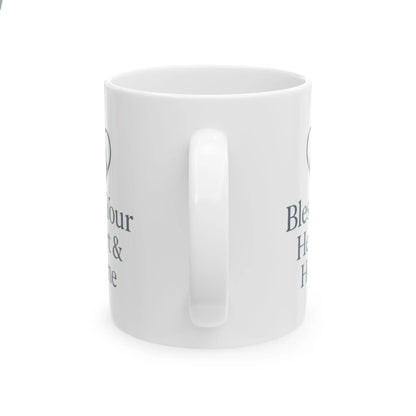 A white ceramic mug with a glossy finish, shown from a side angle on a white background. The mug features dark gray text partially visible on both sides, including the words 'Bless' and 'Home'.