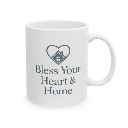 A white ceramic mug with a dark gray printed design featuring a heart outline containing a small house icon and the text 'Bless Your Heart & Home' on a clean white background.