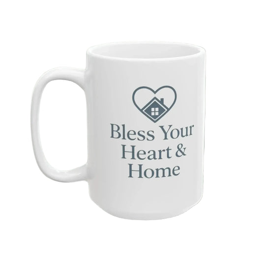 A white ceramic coffee mug with a dark gray printed design featuring a heart-shaped house icon and the text 'Bless Your Heart & Home'.