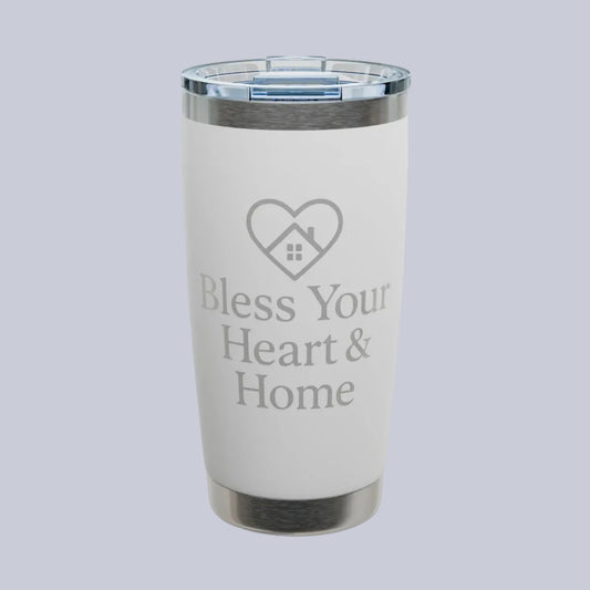 A white insulated tumbler with a clear lid and silver metal trim, featuring the text 'Bless Your Heart & Home' and a heart-shaped house graphic on the front. A small 'Comfort Colors' logo is visible in the top-left corner.