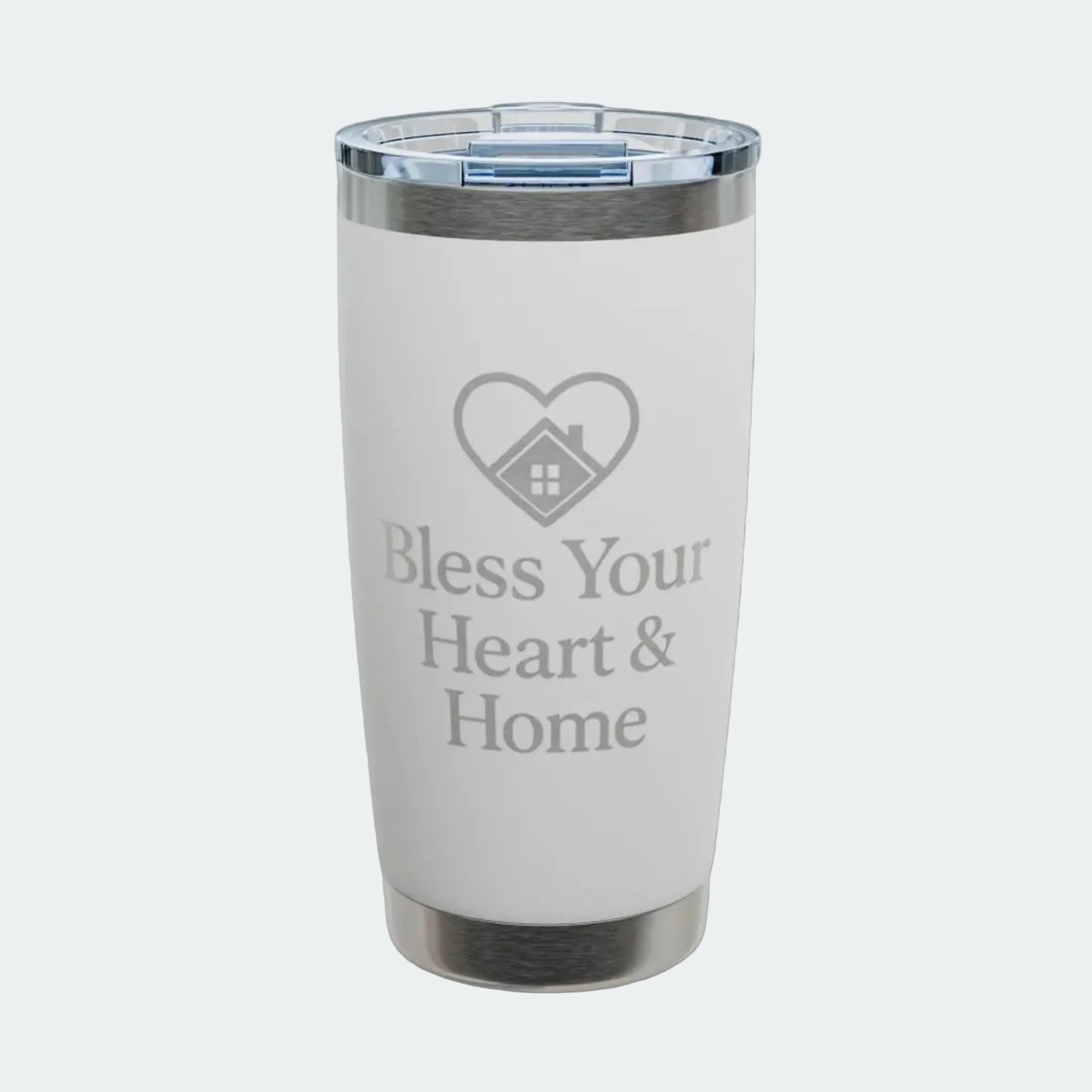 A white insulated tumbler with a clear lid, featuring a gray laser-engraved heart-with-house icon and the text 'Bless Your Heart & Home' on the front. The tumbler is shown on a clean white background with a subtle shadow.