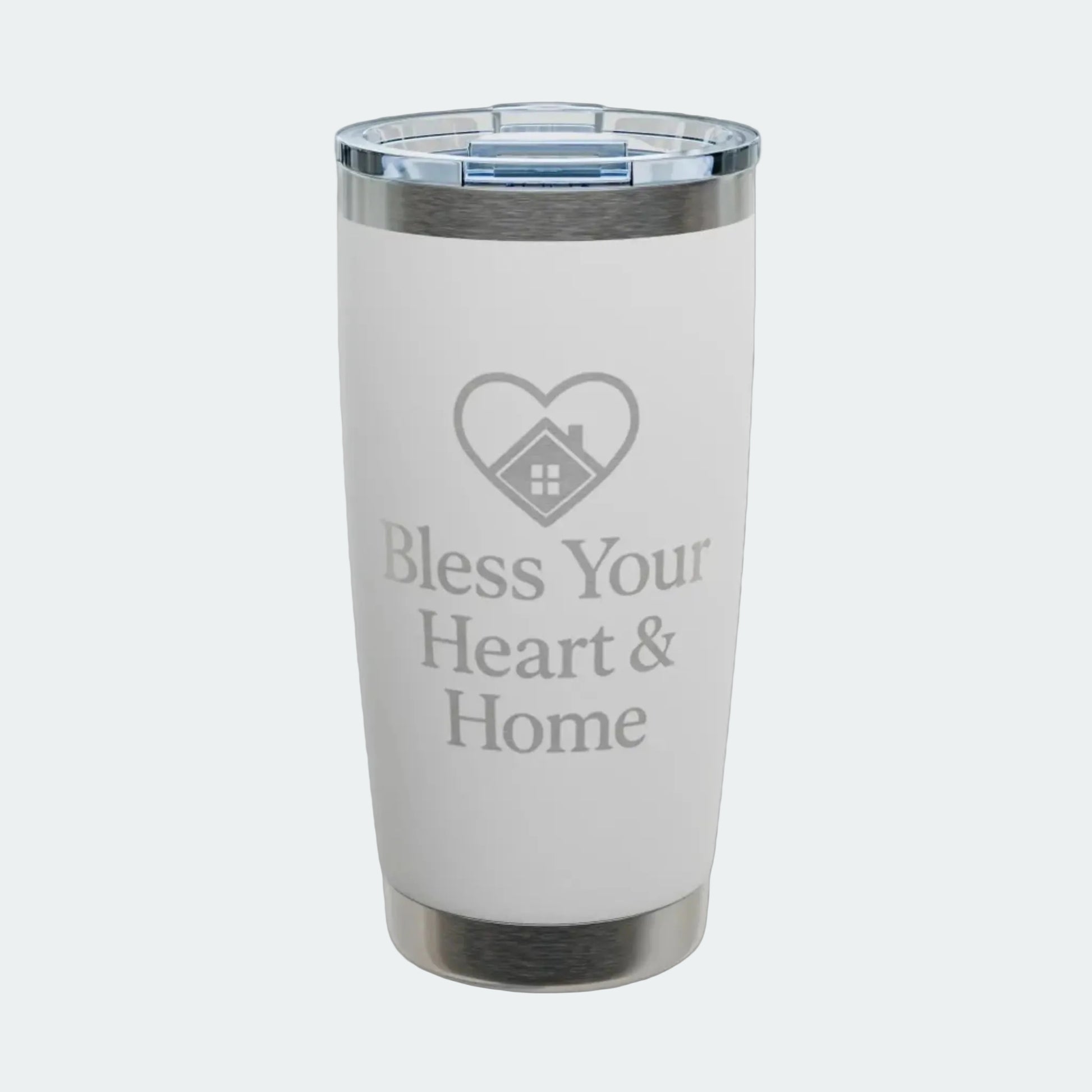 A white insulated tumbler with a clear lid, featuring a gray laser-engraved heart-with-house icon and the text 'Bless Your Heart & Home' on the front. The tumbler is shown on a clean white background with a subtle shadow.
