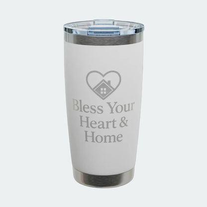 A white insulated tumbler with a clear lid, featuring a gray laser-engraved heart-with-house icon and the text 'Bless Your Heart & Home' on the front. The tumbler is shown on a clean white background with a subtle shadow.