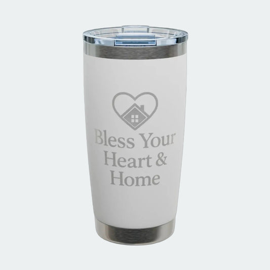 A white insulated tumbler with a clear lid, featuring a gray laser-engraved heart-with-house icon and the text 'Bless Your Heart & Home' on the front. The tumbler is shown on a clean white background with a subtle shadow.