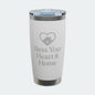 A white insulated tumbler with a clear lid, featuring a gray laser-engraved heart-with-house icon and the text 'Bless Your Heart & Home' on the front. The tumbler is shown on a clean white background with a subtle shadow.