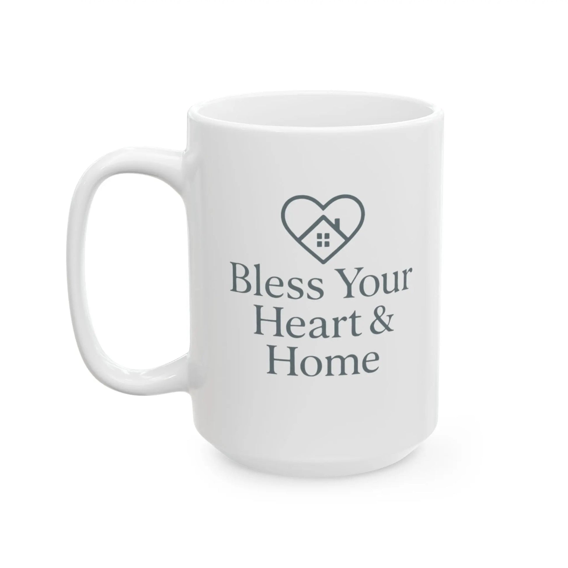 A white ceramic coffee mug with a dark gray printed design featuring a heart-shaped house icon and the text 'Bless Your Heart & Home' on a clean white background.