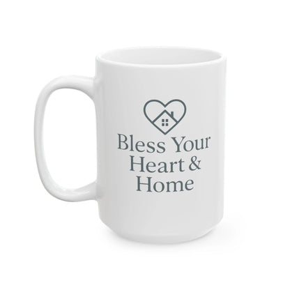 A white ceramic coffee mug with a dark gray printed design featuring a heart-shaped house icon and the text 'Bless Your Heart & Home' on a clean white background.