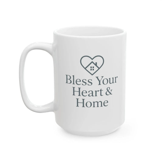 A white ceramic coffee mug with a dark gray printed design featuring a heart-shaped house icon and the text 'Bless Your Heart & Home' on a clean white background.
