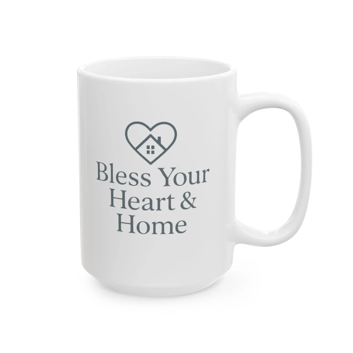 A white ceramic mug with a dark gray printed design featuring a heart outline with a small house inside and the text 'Bless Your Heart & Home' on the front, set against a plain white background.