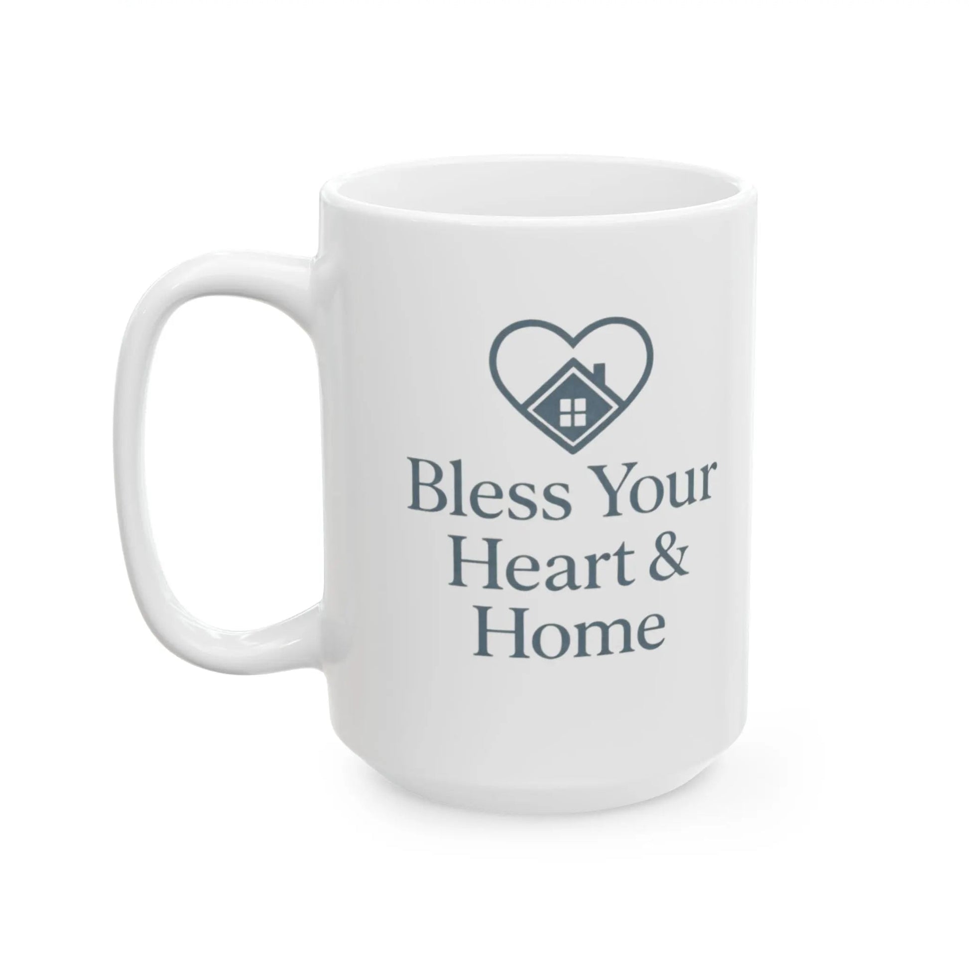 A white ceramic coffee mug with a dark gray printed design featuring a heart-shaped house icon and the text 'Bless Your Heart & Home'.