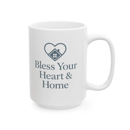 A white ceramic mug with a dark gray printed design featuring a heart-shaped house icon and the text 'Bless Your Heart & Home' on a clean white background.