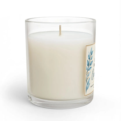 A single-wick candle in a clear glass jar with creamy off-white wax, featuring a decorative label with blue botanical leaves and gold border details, set against a plain white background.