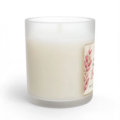 A frosted glass jar candle with creamy off-white wax, featuring a decorative label with pink botanical leaves on the side, set against a plain white background.