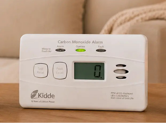 Security camera and carbon monoxide alarm on a table with promotional text about the 'Peace of Mind Bundle'.