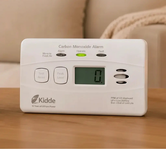 Security camera and carbon monoxide alarm on a table with promotional text about the 'Peace of Mind Bundle'.