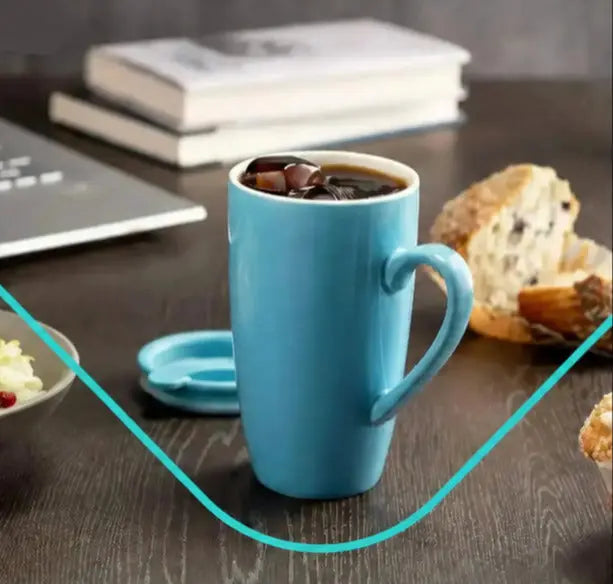 single ceramic coffee mug with lid filled with iced coffee on desk near laptop and food