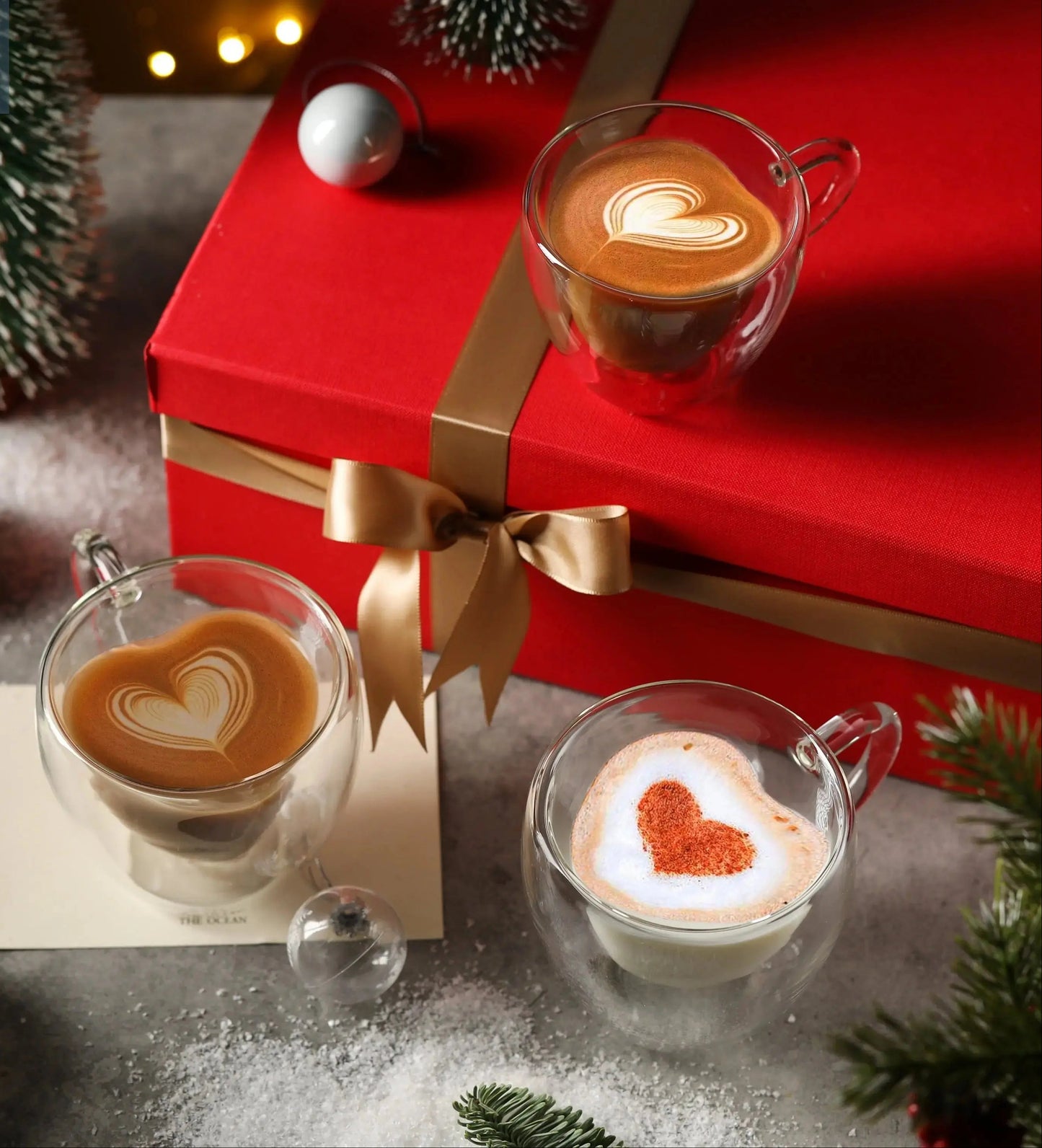 Double wall heart-shaped glass mug filled with coffee shown in cozy holiday gift setting with multiple mugs
