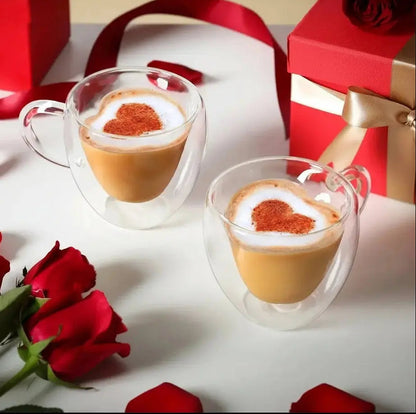 Double wall heart-shaped glass mugs filled with coffee shown in romantic gift setting with roses and red boxes
