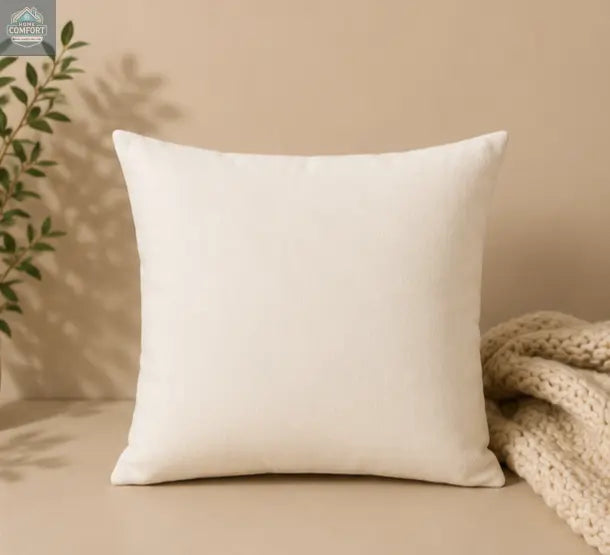 Beige pillow on a beige surface with a plant and textured fabric in the background