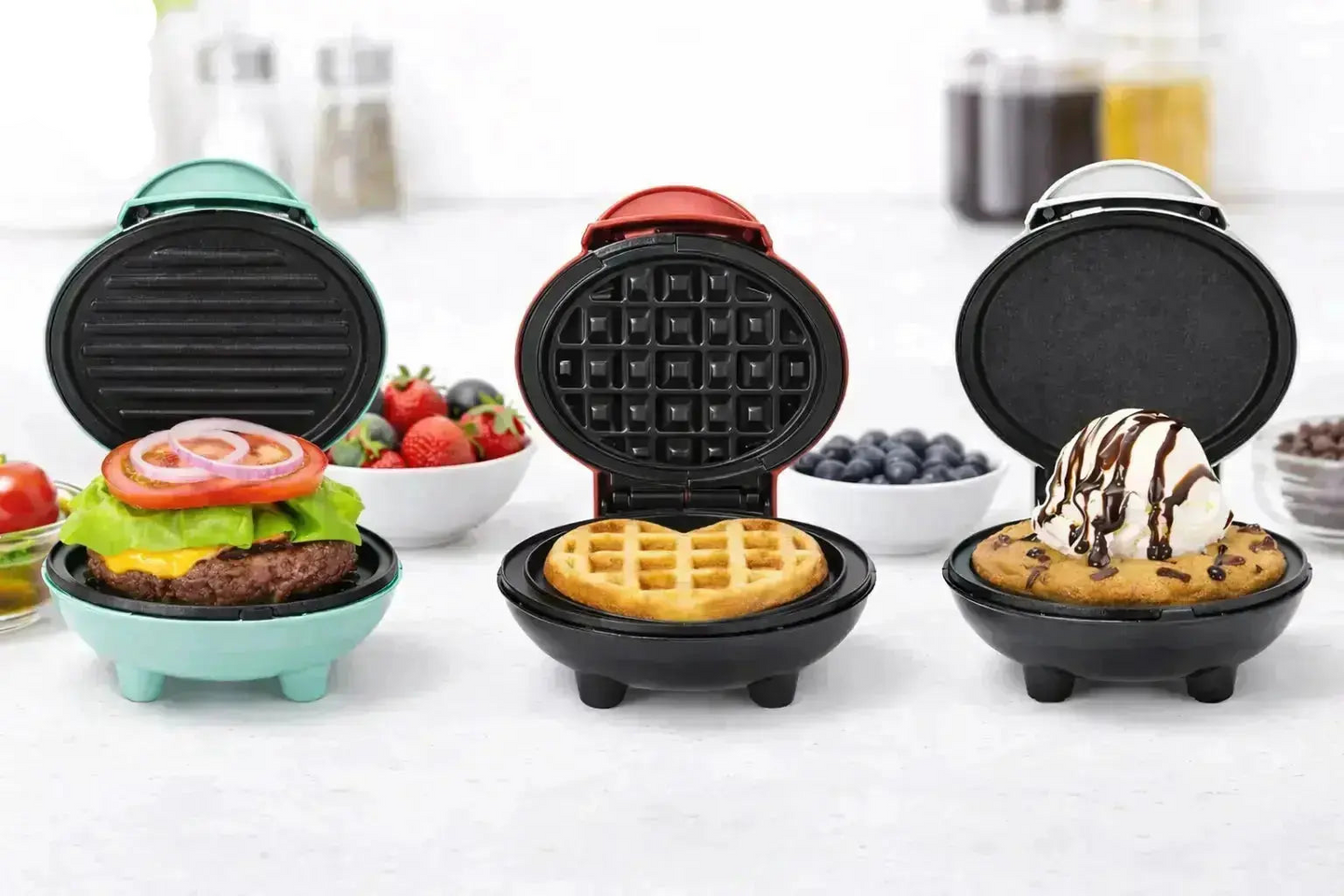 Three mini waffle makers open on a kitchen counter showing burger, waffle, and dessert cooking examples.