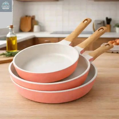 3-piece coral nonstick frying pan set stacked with wooden handles on kitchen countertop