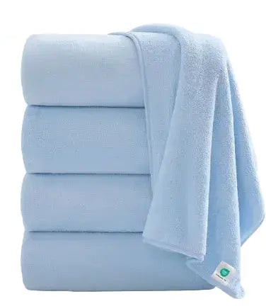 A stack of four light blue folded towels with one towel draped over the side, shown on a plain white background. A small green and white tag is visible on the corner of the draped towel.