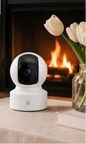 White security camera on a table with a fireplace and flowers in the background