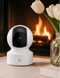 White security camera on a table with a fireplace and flowers in the background