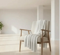 Pearl knit chenille throw blanket draped over a cozy armchair in a warm living room with fireplace