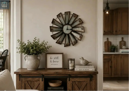 Decorative 14.5" round vintage metal windmill wall clock on a wall above a wooden console table with plants and books.